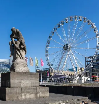 Tauzieher statue of a man securing a thick rope around a bollard, with a Ferris wheel and waterfront buildings in the background.