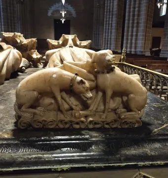 Detail of the Tomb of Charles III and Eleanor showing two sculpted dogs at the base of the monument, with draped stone effigies behind them.