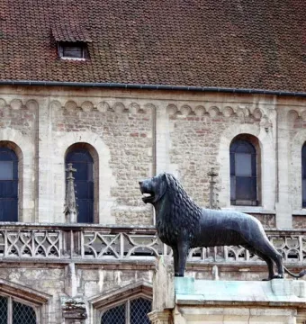 The Brunswick Lion statue stands on a stone pedestal in front of a historic stone building.