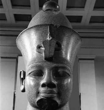Colossal head of Amenhotep III with a tall crown and damaged neck, displayed on a base.