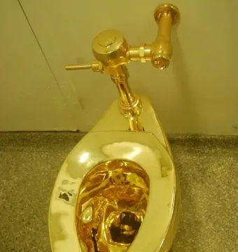 A gleaming gold-colored toilet mounted on a light wall above a speckled gray floor.