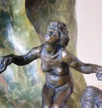 Bronze nude figure from The Wave with outstretched arms against green veined stone.