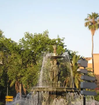 The Three Graces Fountain with a classical sculpture on top, spraying water in a landscaped roundabout.