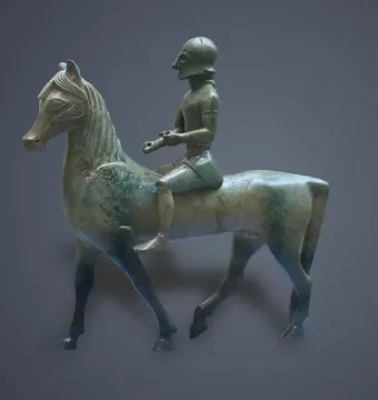 Armento Rider bronze figurine of a helmeted warrior mounted on a horse-like animal, shown in side profile against a gray background.