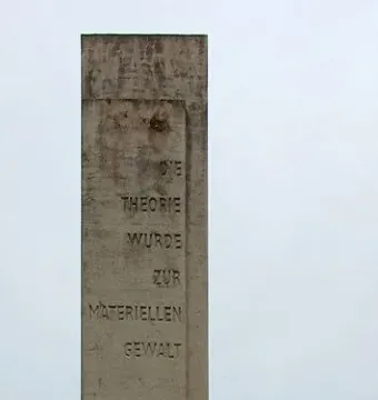 Karl Marx Monument with a carved stone stele and a dark bust on a pedestal in a park setting.