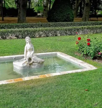 White Mermaid Fountain statue pouring water into a rectangular stone basin in a green park.