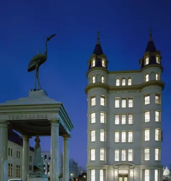 Temperance Fountain beside a brightly lit historic building at twilight, with a stone monument topped by a heron sculpture.