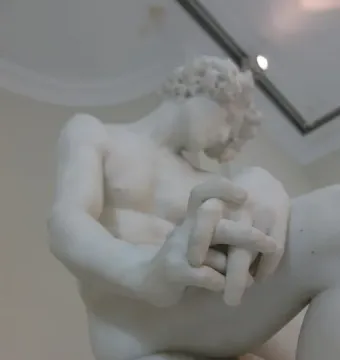 The Exiled, a white marble sculpture of a seated male figure with bowed head and clasped hands.