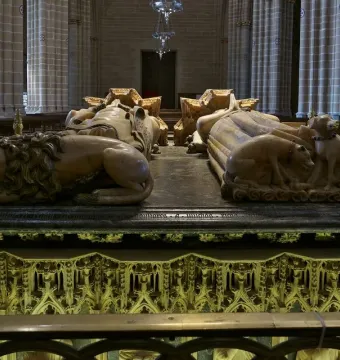 Tomb of Charles III and Eleanor with recumbent stone effigies, a lion at one figure\'s feet and two dogs at the other\'s, in a Gothic cathedral interior.