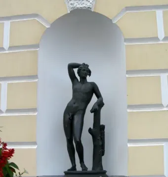 Apollino nude male statue in a white arched niche with a quiver and tree trunk support.