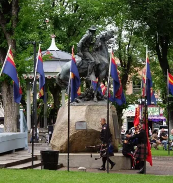 Buckey O\'Neill Monument with a bronze equestrian statue surrounded by flags and people at a ceremony.