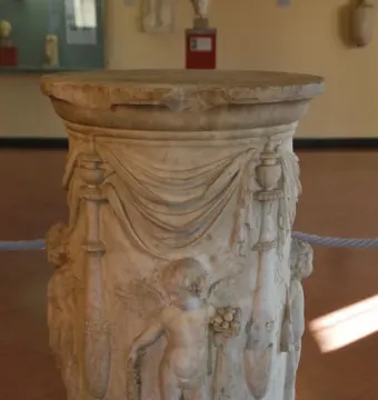 Round marble Four Seasons Altar with carved drapery, decorative pillars, and a winged putto holding grapes and a basket of fruit.