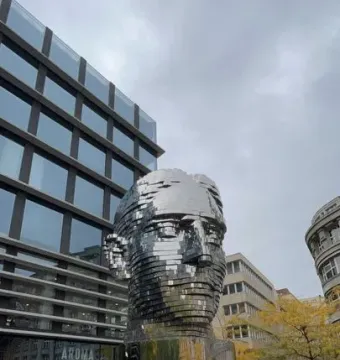 The rotating Head of Franz Kafka sculpture, a reflective segmented metallic head in an urban square.