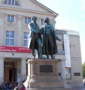 Goethe and Schiller Monument on a tiered stone pedestal in front of a theatre building.