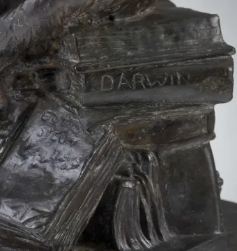 Close-up of Hugo Rheinhold’s Ape With Skull sculpture showing a stack of books with DARWIN on the spine.