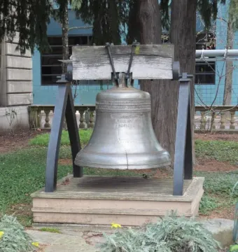 The Liberty Bell displayed on a wooden platform with a dark metal frame, surrounded by trees and ground cover.