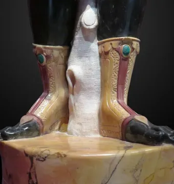 Close-up of the Moor of Borghese statue showing the lower legs, bare feet, and carved boots above a marbled pedestal.