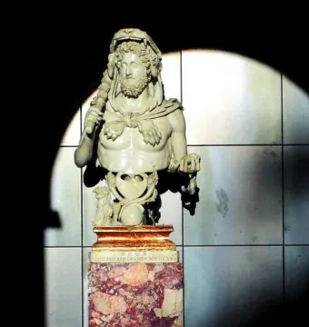 Marble bust of Commodus as Hercules with a lion-skin headdress and club, displayed on a reddish-brown pedestal.