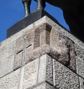 Stone plinth of the Grunwald Monument with red and grey panels, seen from below with the bronze legs of the equestrian statue above.