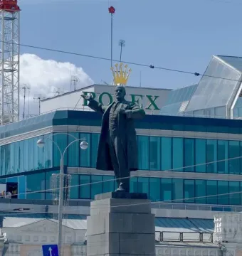 Lenin Monument on a stone pedestal with a modern glass building behind it