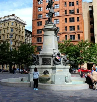 The Maisonneuve Monument stands in a paved square, with a tall stone column topped by a dark statue and smaller figures at the base fountain.