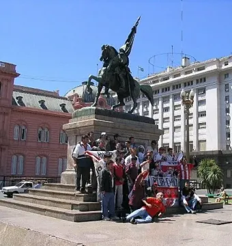 Manuel Belgrano equestrian statue on a tall pedestal in a city square, with people gathered around the base.