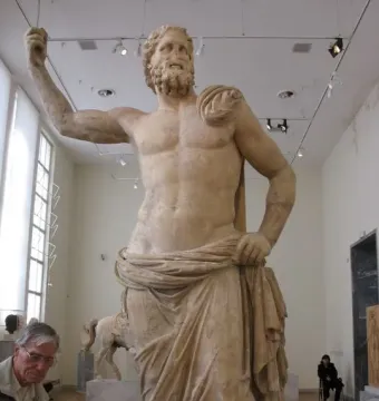 Poseidon of Melos marble statue in a museum hall, with a raised arm and draped lower body