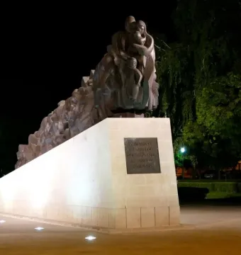 The Train of Pain monument lit at night, showing a long sculpture of human figures on a stone pedestal.