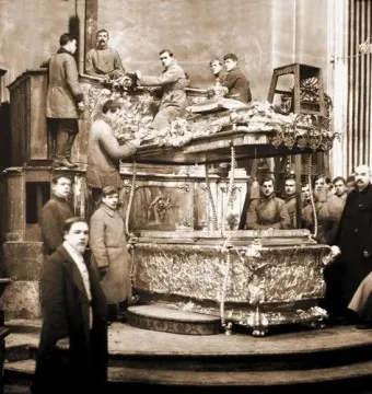Men dismantle the ornate Alexander Nevsky reliquary on a raised platform in a black-and-white photograph.
