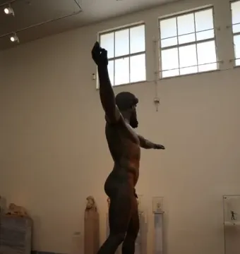 Artemision Bronze statue of a nude bearded man with one arm raised and the other outstretched in a museum gallery.