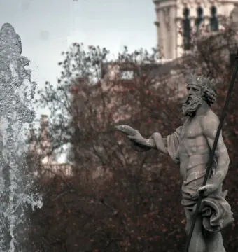 Fountain of Neptune statue with a crowned bearded figure holding a trident beside a strong water jet.
