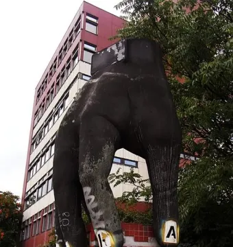 The Hand with Watch sculpture, a dark weathered hand mounted on a graffiti-covered pedestal in an urban setting.