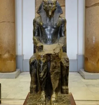 Khafre Enthroned, a dark stone statue of a seated pharaoh on an ornate throne with a falcon carved around the back.