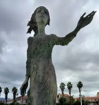 La madre del emigrante bronze statue of a gaunt woman with one arm outstretched in a plaza