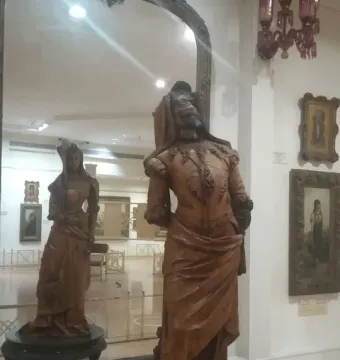 Mephistopheles and Margaretta carved in a tall wooden double-sided statue, with a mirror showing the female figure behind the male figure.