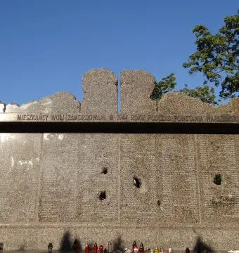 Granite Monument to Victims of the Wola Massacre with engraved Polish text and memorial candles at the base.