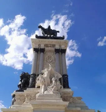 Alfonso XII Monument with a dark equestrian statue atop a multi-tiered marble base under a blue sky.