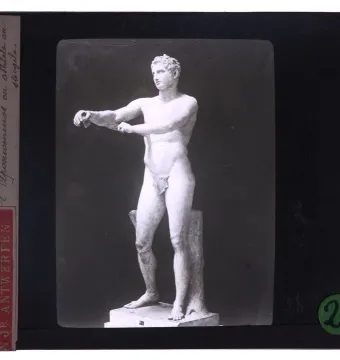 Classical Apoxyomenos statue of a nude male athlete extending his arms in a scraping pose against a dark background.