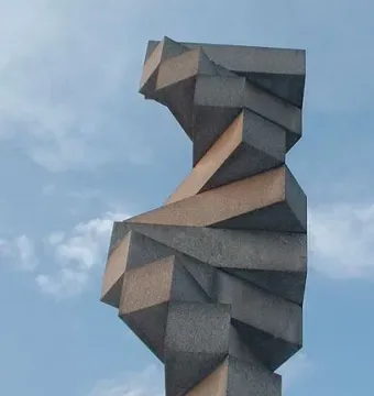 Endlose Treppe, a tall helical sculpture of stacked grey stone blocks against a blue sky.