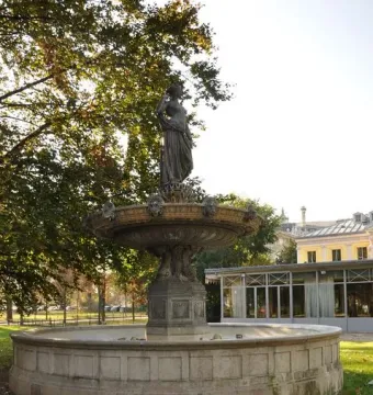Diana Fountain with a robed female figure atop a multi-tiered stone and metal monument on a grassy lawn.