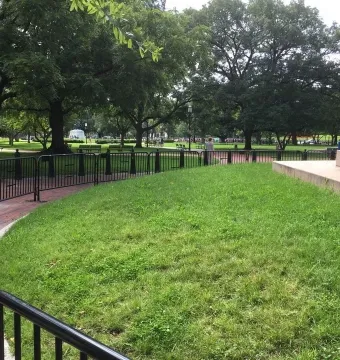 Partial view of the Major General Friedrich Wilhelm von Steuben monument on a stone base beside a grassy park and brick path.