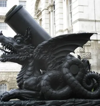 The Cádiz Memorial shows a large mortar mounted on a dark dragon-like sculpture, with a white building and equestrian statue in the background.