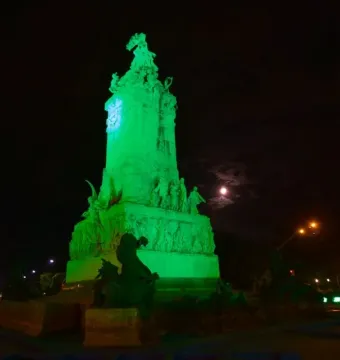 Monument to the Carta Magna and Four Regions of Argentina lit in green at night, with a full moon beside it.