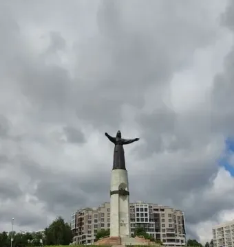 Mother Patroness statue with outstretched arms on a tall pedestal above a stepped plaza.