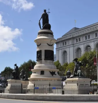 The rear of the Pioneer Monument, a multi-tiered stone monument topped by a robed figure holding a shield and spear, with bronze statues around the base.