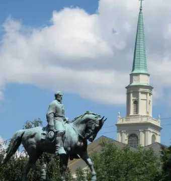 Robert E. Lee Monument, a green-patinated equestrian statue on a stone pedestal with a church steeple and trees behind it.