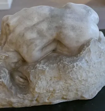 Rodin\'s Danaid sculpture showing a nude figure bent low over a rough base.