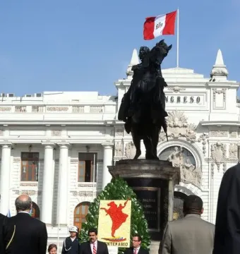 Equestrian statue of Simón Bolívar in front of a grand white building, with a Peruvian flag above and a floral wreath at the base.