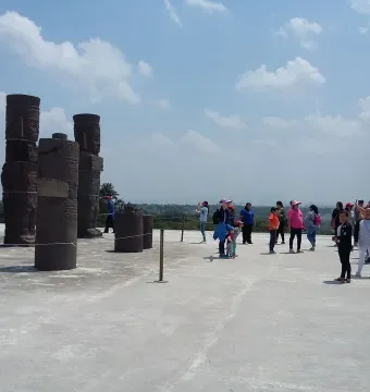 Tall stone Atlantean Figures at Tula standing on a wide plaza with tourists and a bright blue sky overhead.
