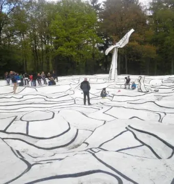 Jardin d\'émail with a white undulating platform, black lines, and a tall abstract white structure in front of a forest.